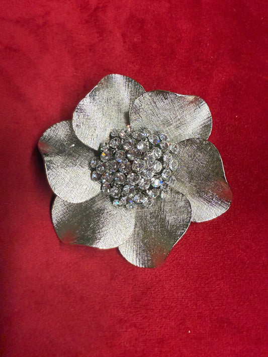 Silver flower-shaped brooch with rhinestones on a red background
