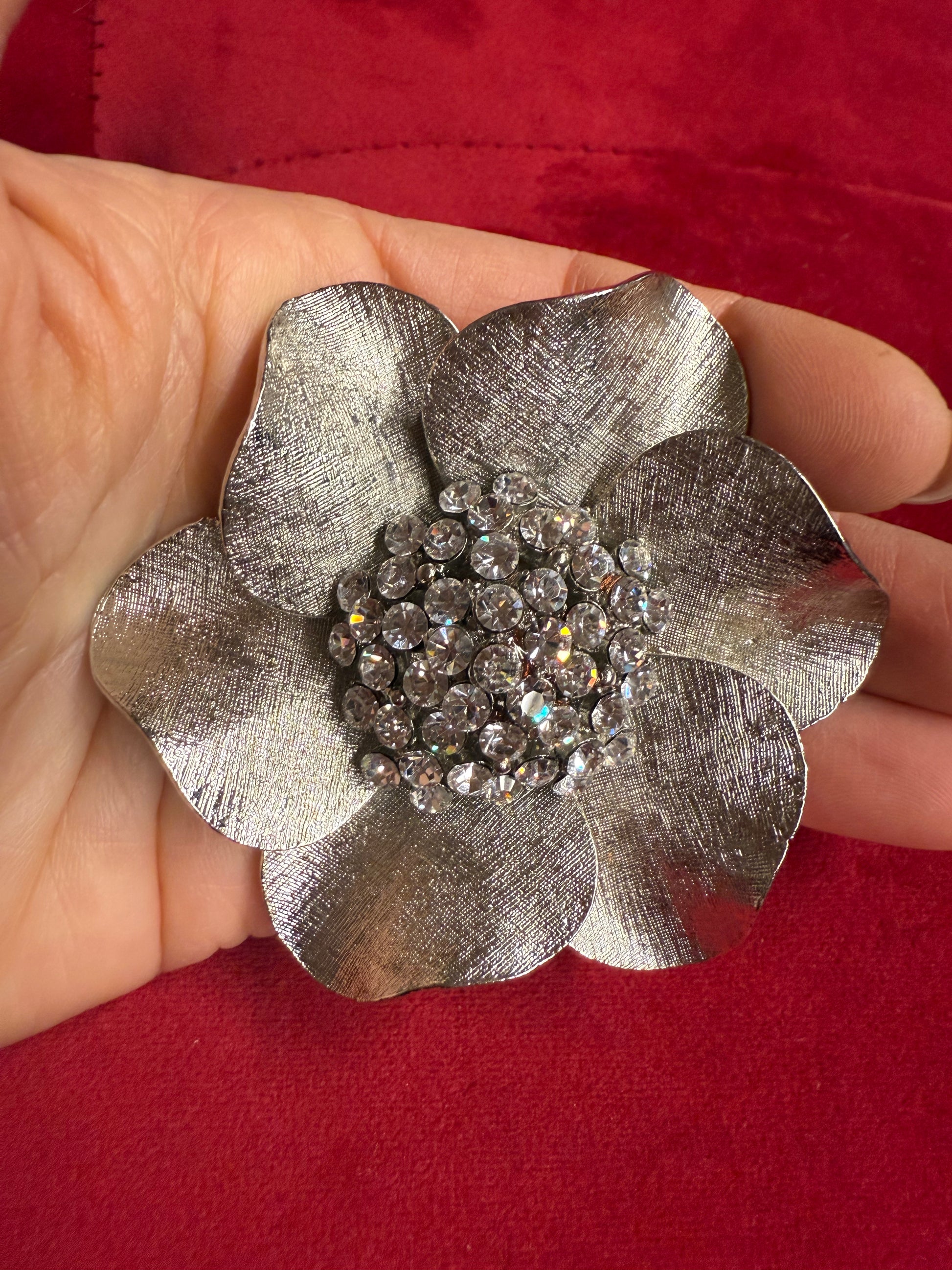 Silver flower-shaped brooch with gemstones held against a red background